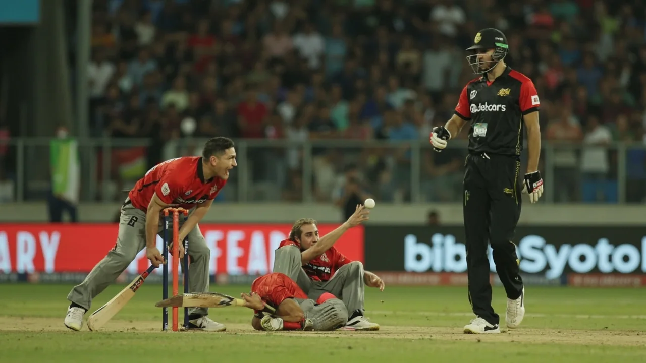 Fielders in catching positions and a captain gesturing field changes during a Twenty20 match in the Caribbean, with batsmen conferring mid-pitch.